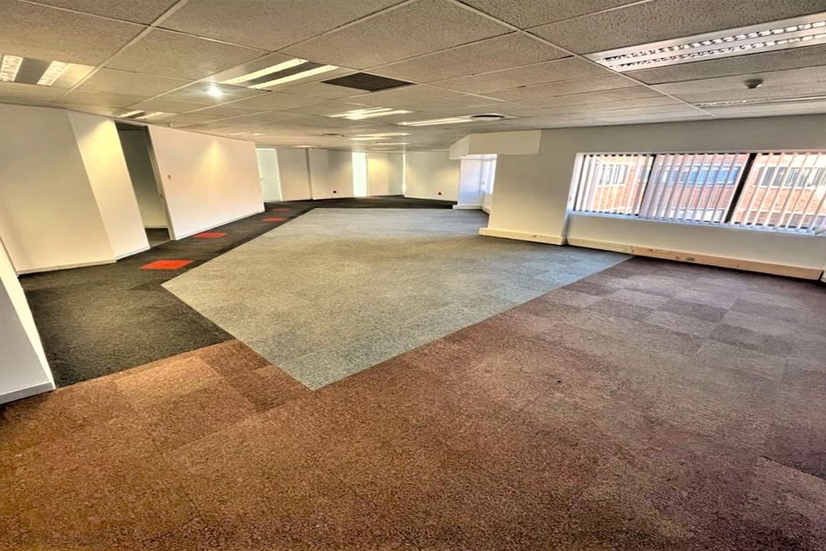 Spacious open-plan office area featuring suspended ceilings, recessed lighting, and multi-colored carpet tiles, offering a versatile workspace layout.
