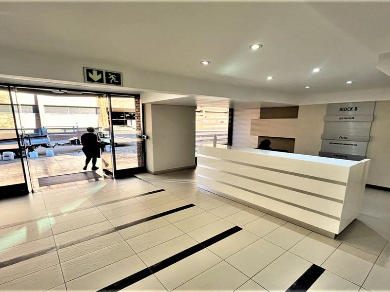 Modern office building entrance lobby featuring a sleek reception desk, tiled flooring, recessed lighting, and clear directional signage for building levels.