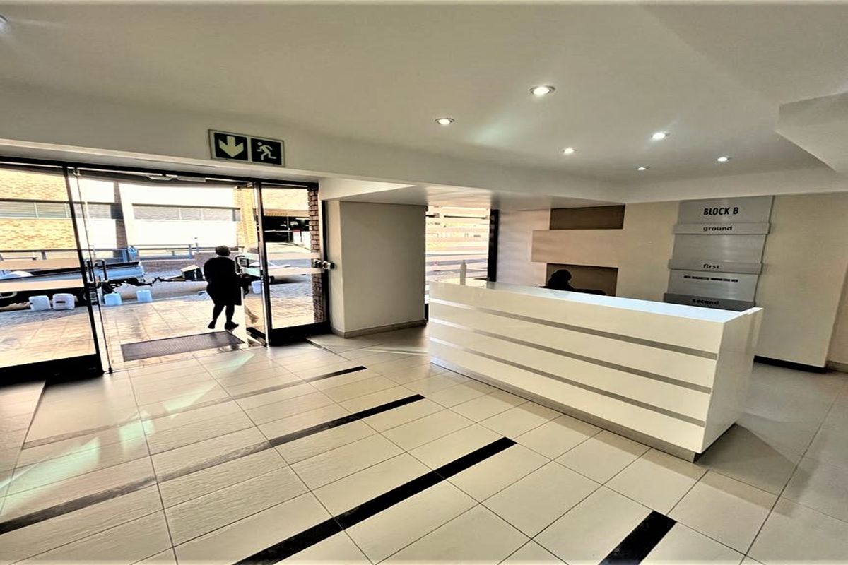 Modern office building entrance lobby featuring a sleek reception desk, tiled flooring, recessed lighting, and clear directional signage for building levels.