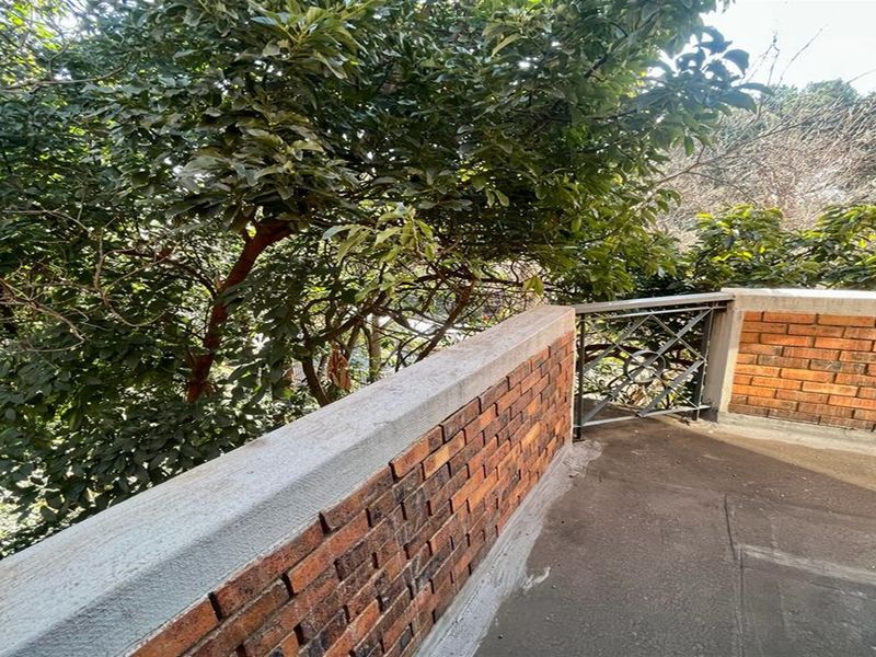 An outdoor balcony featuring a brick parapet wall with concrete coping and metal railing, surrounded by mature trees.