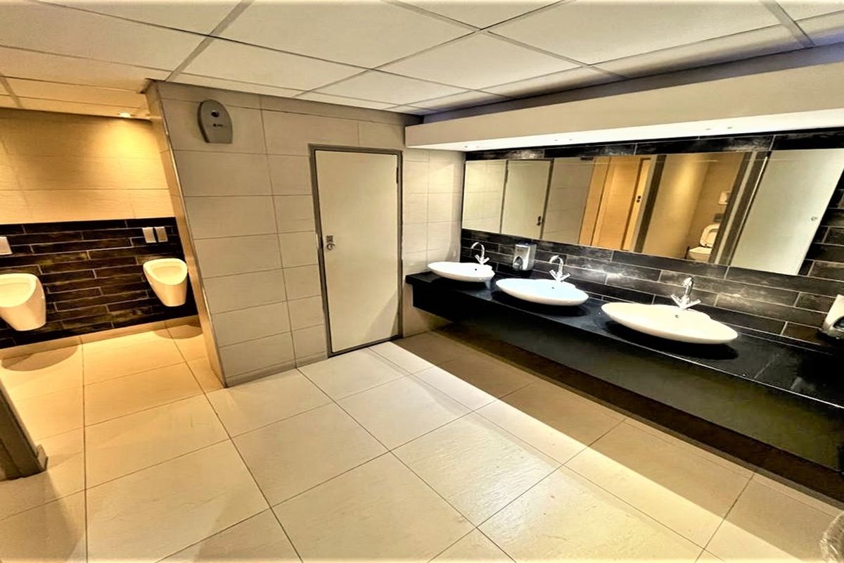 A modern, well-maintained office restroom featuring multiple vanity basins, wall-mounted mirrors, and a dedicated urinal area with contemporary tiling.