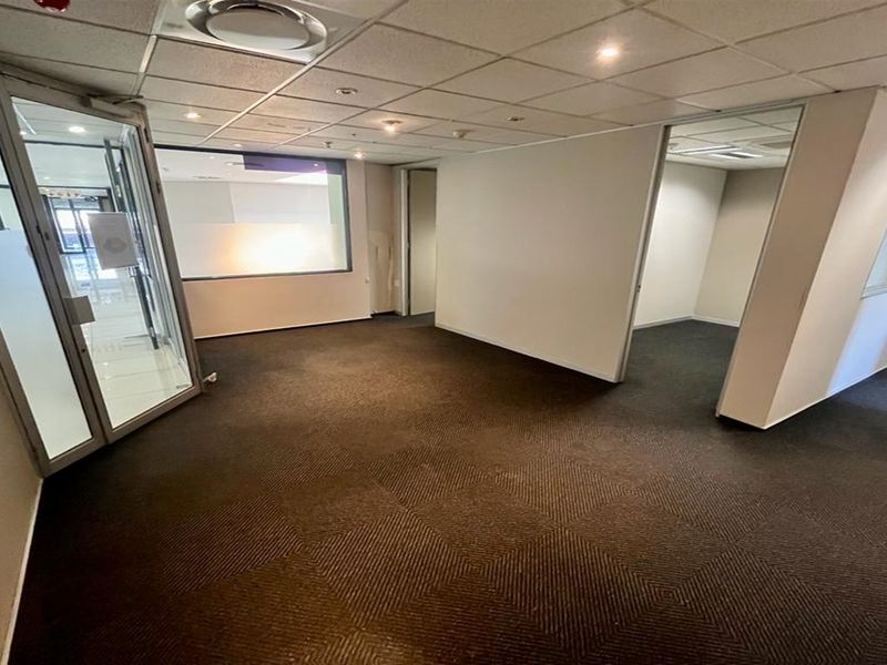 An empty office space featuring a suspended ceiling, recessed lighting, and glass partitions, providing a versatile layout for professional use.
