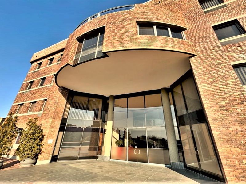 A professional office building exterior featuring a distinctive curved brick facade, large glass entrance doors, and a covered portico area.