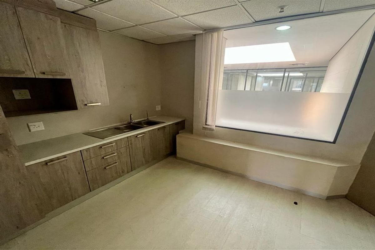 A functional office kitchenette featuring wood-look cabinetry, a stainless steel sink, and a large frosted glass window partition.