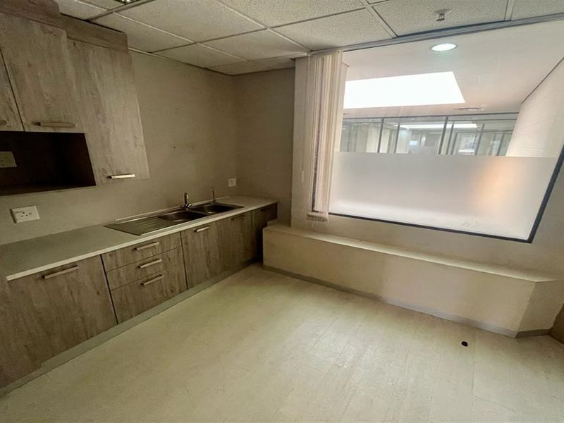 A functional office kitchenette featuring wood-look cabinetry, a stainless steel sink, and a large frosted glass window partition.
