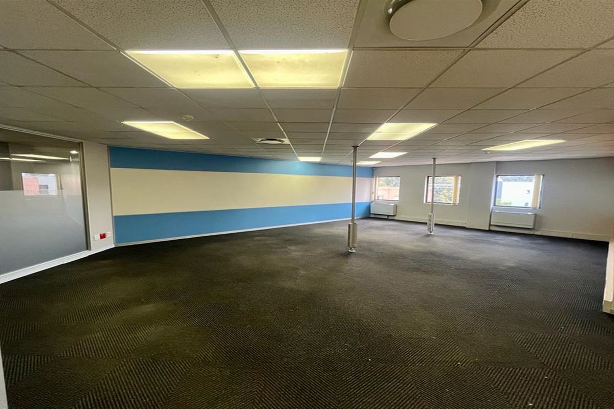 An open-plan office space featuring a suspended ceiling, recessed lighting, carpeted flooring, and structural support columns, offering a versatile workspace layout.