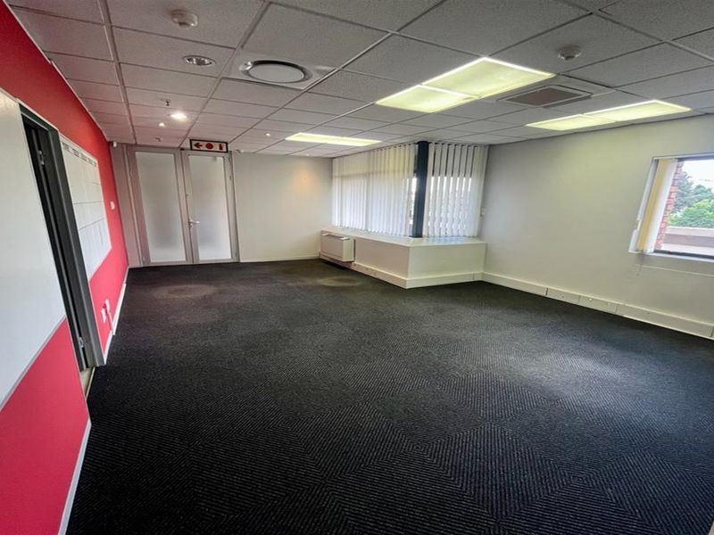 A vacant office space featuring a suspended ceiling, recessed lighting, vertical blinds, and dark carpeted flooring, suitable for a professional workspace.