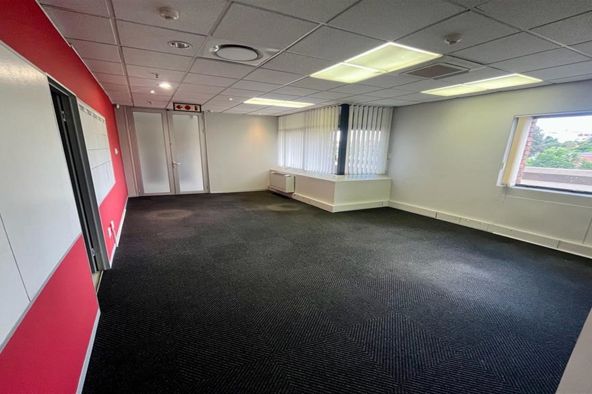 A vacant office space featuring a suspended ceiling, recessed lighting, vertical blinds, and dark carpeted flooring, suitable for a professional workspace.