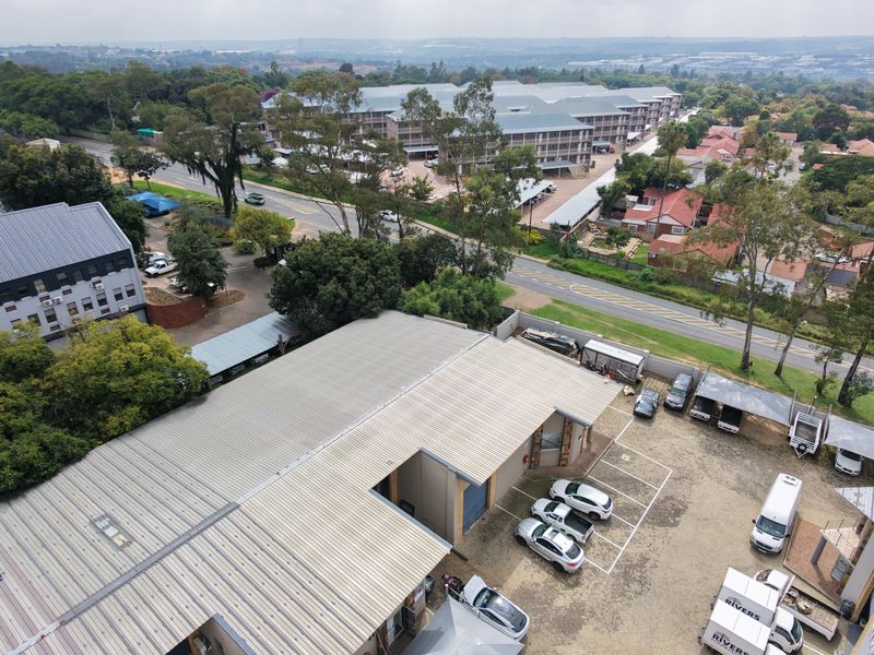 Aerial view of an industrial property featuring a metal roof, solar panels, and a paved parking area with multiple carport structures.