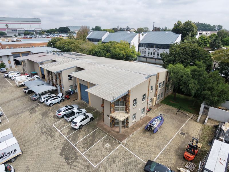 Aerial view of an industrial property featuring a large warehouse building, corrugated metal roofing, and an extensive paved parking area.