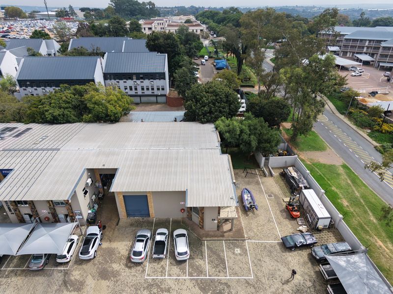 Aerial view of an industrial property featuring a corrugated metal roof, paved parking area, and roller shutter access doors within a secure complex.