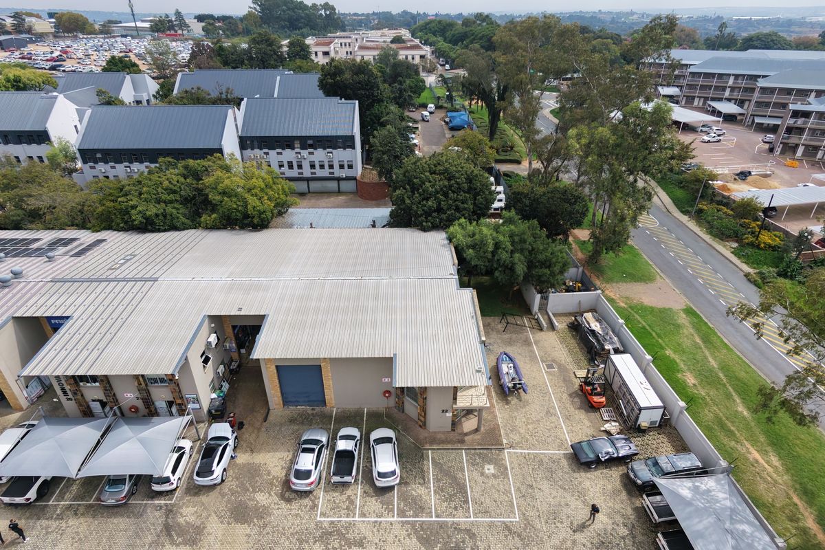 Aerial view of an industrial property featuring a corrugated metal roof, paved parking area, and roller shutter access doors within a secure complex.