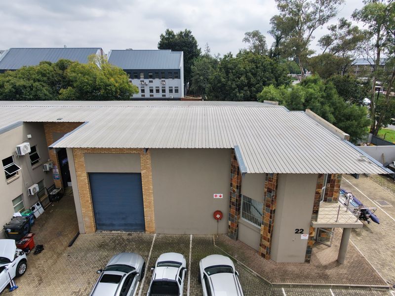 Aerial view of an industrial property featuring a corrugated metal roof, roller shutter door, and paved parking area.