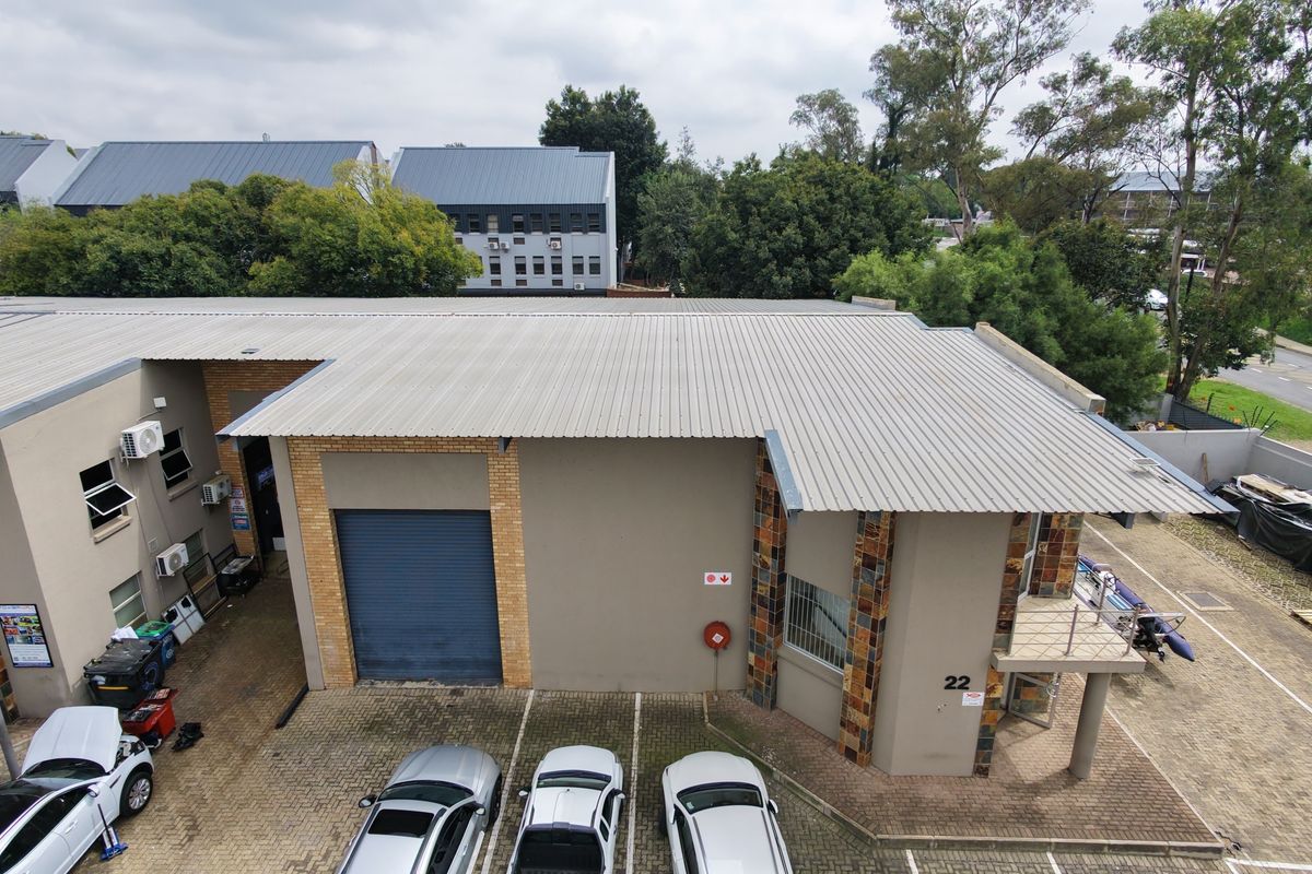 Aerial view of an industrial property featuring a corrugated metal roof, roller shutter door, and paved parking area.