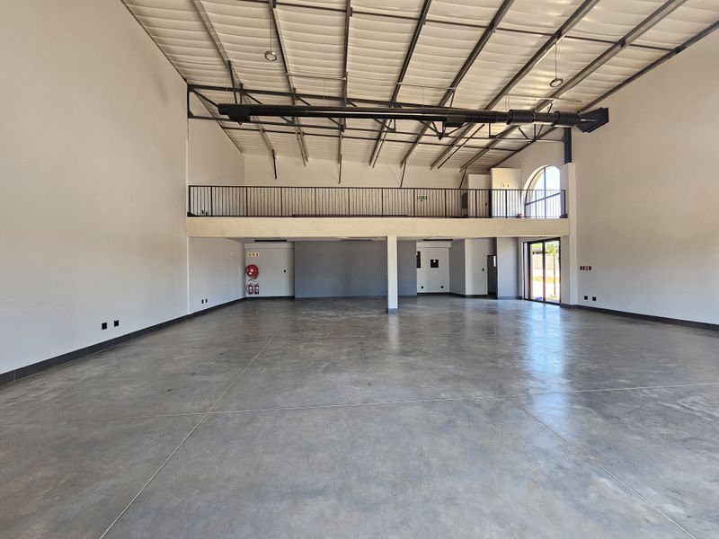 Spacious open-plan retail unit featuring polished concrete flooring, high exposed industrial ceilings, and a mezzanine level with metal railing.