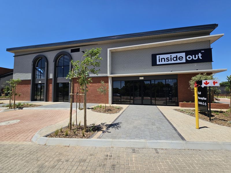 Modern retail building facade featuring brickwork, large glass storefronts, arched windows, and paved entrance area with professional signage.
