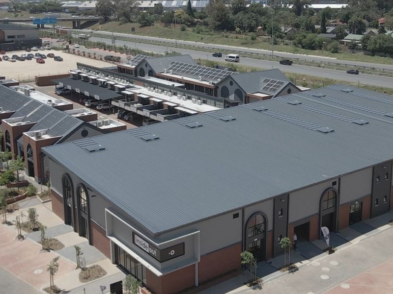 Aerial view of a modern retail complex featuring metal roofing, brick and plaster facade, and integrated parking facilities.