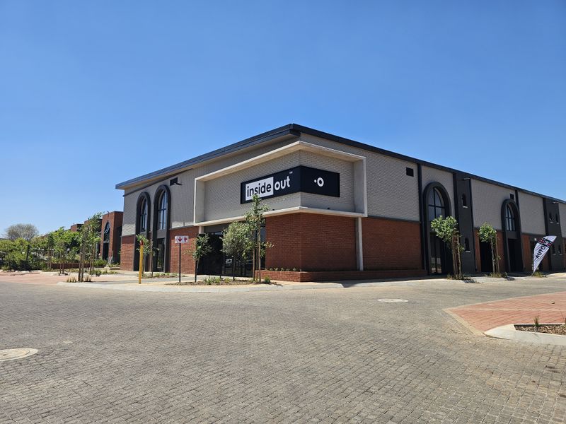 Modern commercial retail building featuring a combination of red brick and grey textured facade with arched window detailing and paved exterior surroundings.