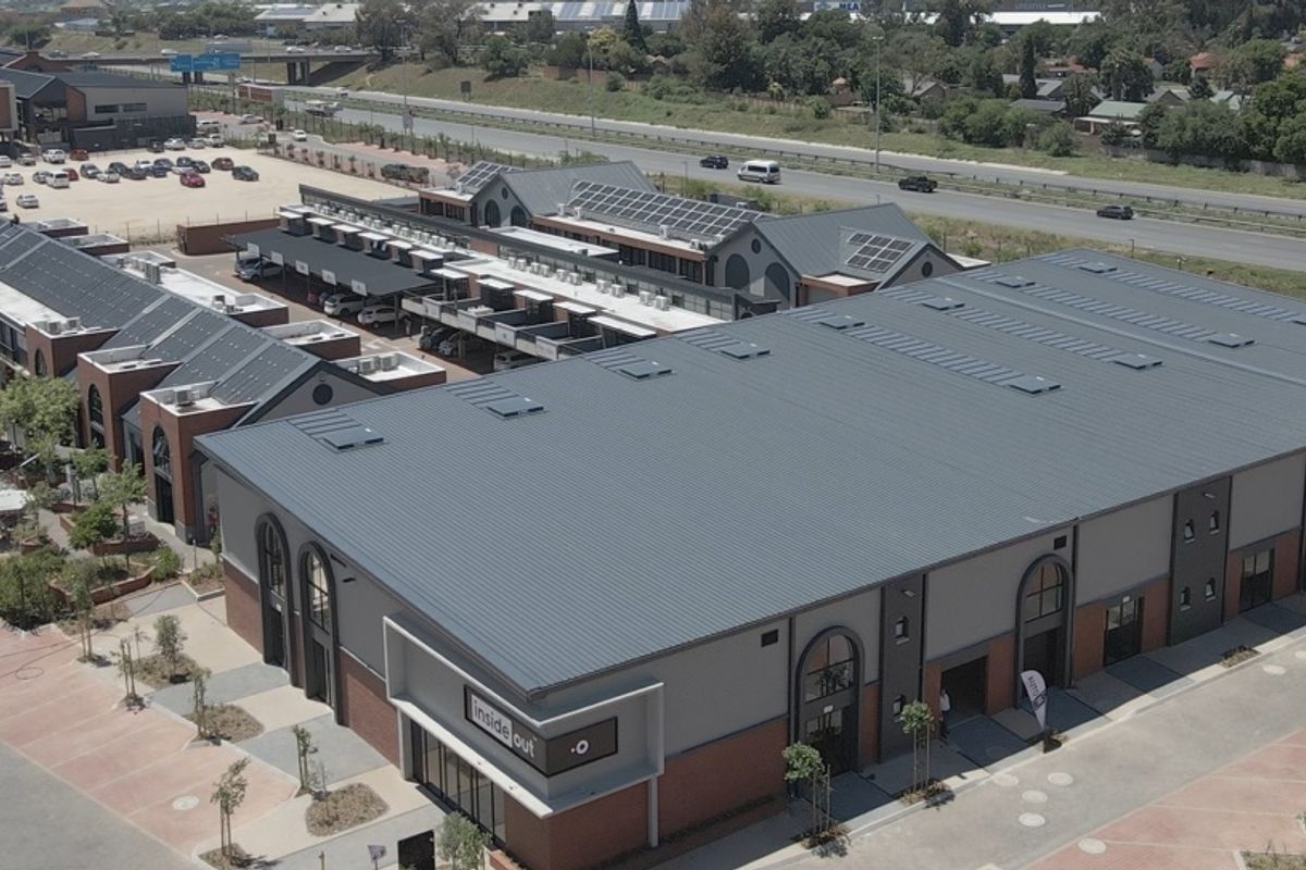 Aerial view of a modern retail complex featuring metal roofing, brick and plaster facade, and integrated parking facilities.