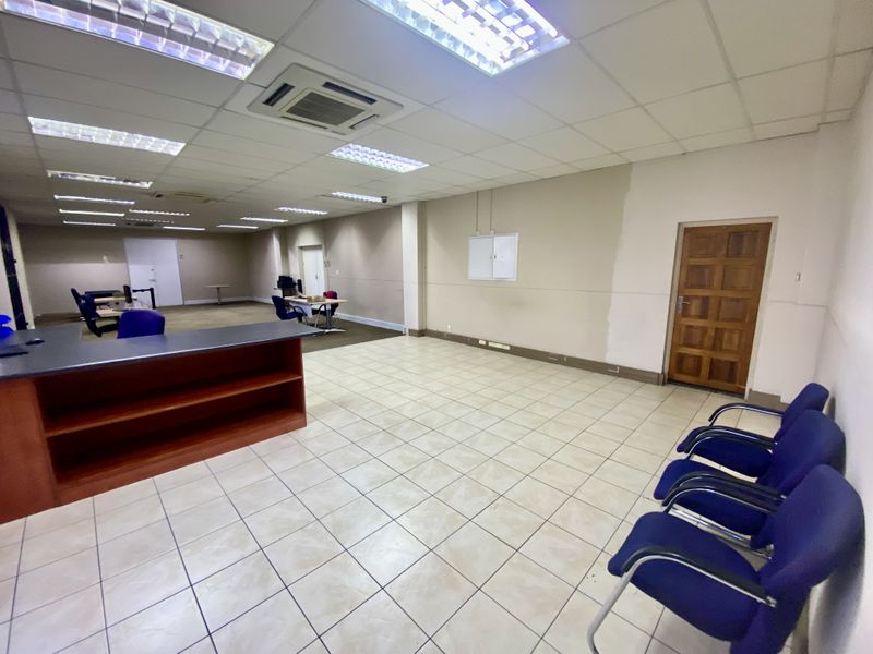 Spacious industrial office area featuring tiled flooring, suspended ceilings with recessed lighting, integrated air conditioning, and a built-in reception counter.