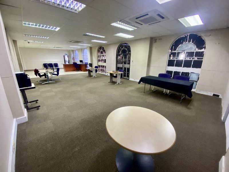 Spacious open-plan office area featuring carpeted flooring, recessed lighting, and arched windows, suitable for a flexible workspace layout.