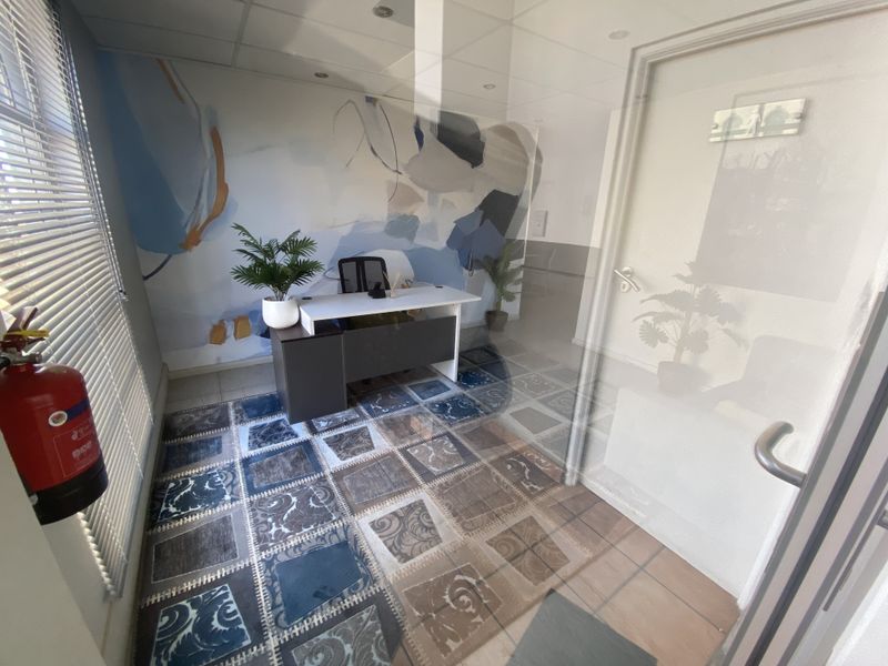 A compact office space featuring tiled flooring, recessed lighting, and venetian blinds, providing a functional workspace environment.