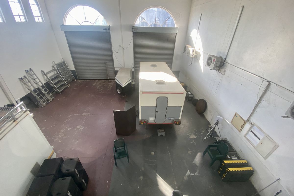 Spacious industrial garage featuring high ceilings with exposed trusses, dual roller shutter doors, arched windows, and wall-mounted air conditioning units.