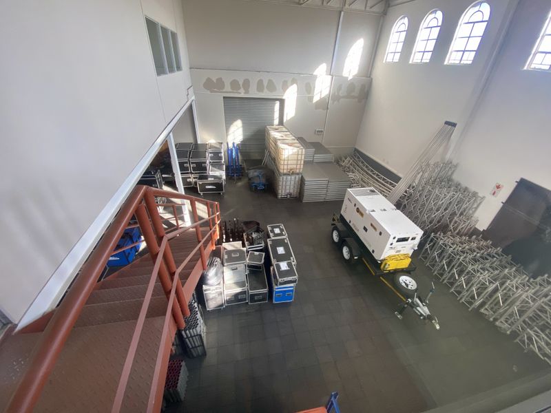 Spacious industrial utility area featuring high ceilings, arched windows, a metal staircase, and a large roller shutter door for easy access.