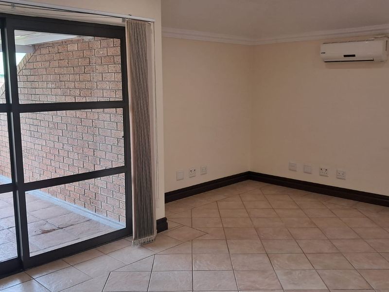 An empty office space featuring tiled flooring, a wall-mounted air conditioning unit, and large sliding glass doors leading to a private balcony.