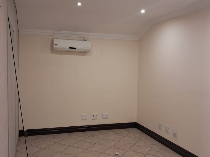 A clean, empty office space featuring tiled flooring, recessed ceiling lighting, and a wall-mounted air conditioning unit.