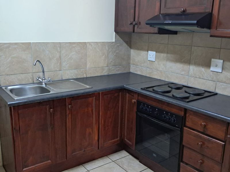A functional office kitchenette featuring dark wood cabinetry, a stainless steel sink, a built-in oven, and a black electric hob with an extractor fan.