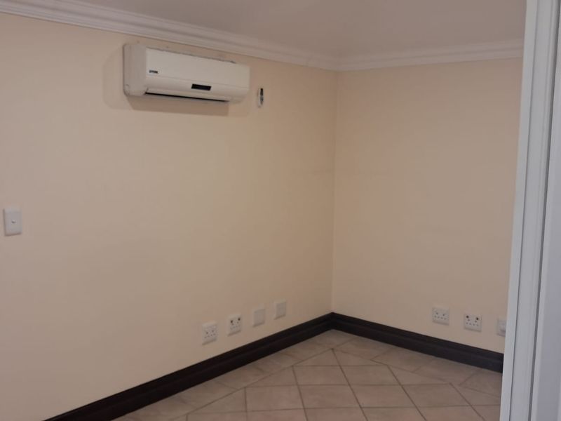 A clean, empty office space featuring tiled flooring, crown molding, and a wall-mounted air conditioning unit.