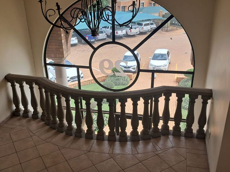 A landing area featuring a large arched window with decorative ironwork, stone balustrade railing, and tiled flooring overlooking the parking area.