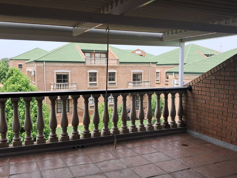 A covered balcony featuring a classic balustrade railing, tiled flooring, and brick wall finishes, offering an elevated view of the surrounding office complex.