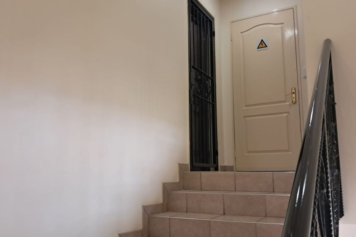 A staircase with tiled steps and a metal handrail leading to a landing with a security gate and an electrical room door.
