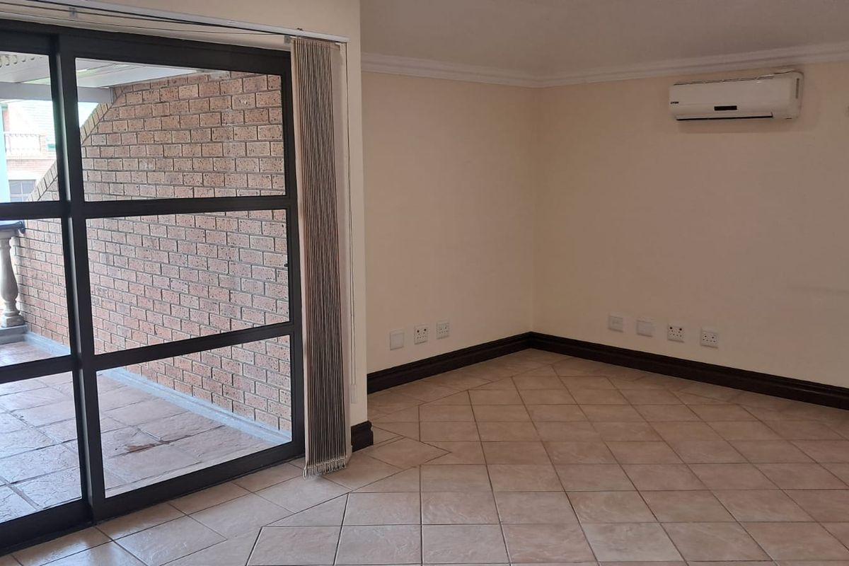 An empty office space featuring tiled flooring, a wall-mounted air conditioning unit, and large sliding glass doors leading to a private balcony.