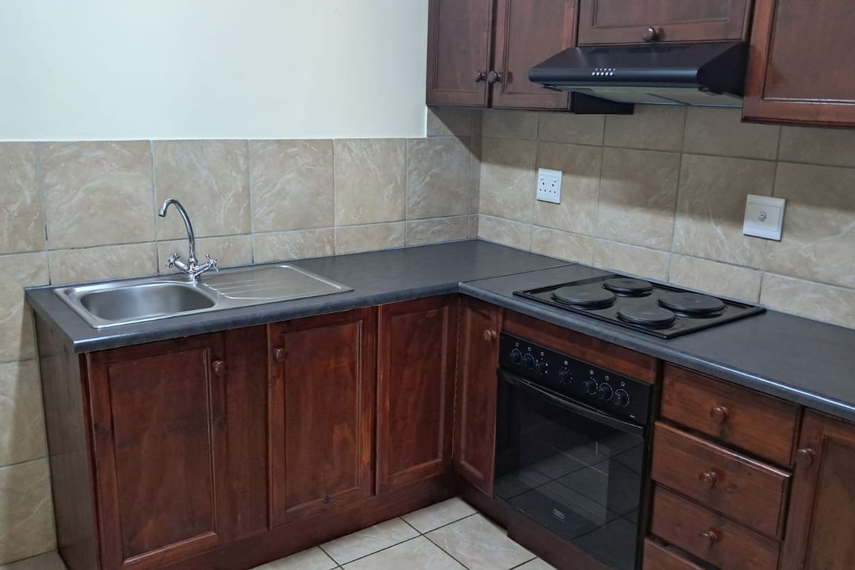 A functional office kitchenette featuring dark wood cabinetry, a stainless steel sink, a built-in oven, and a black electric hob with an extractor fan.