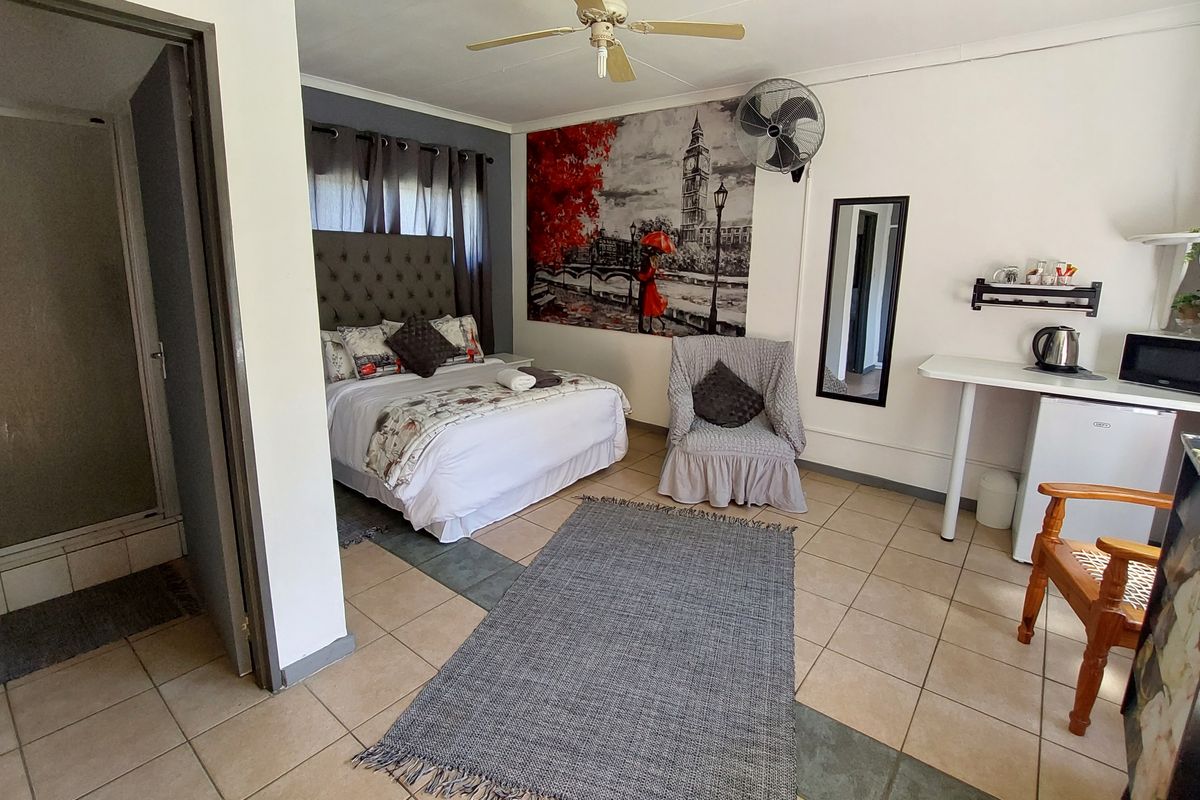 A functional bedroom featuring tiled flooring, a ceiling fan, wall-mounted fan, and an en-suite bathroom, providing a practical layout for guest accommodation.