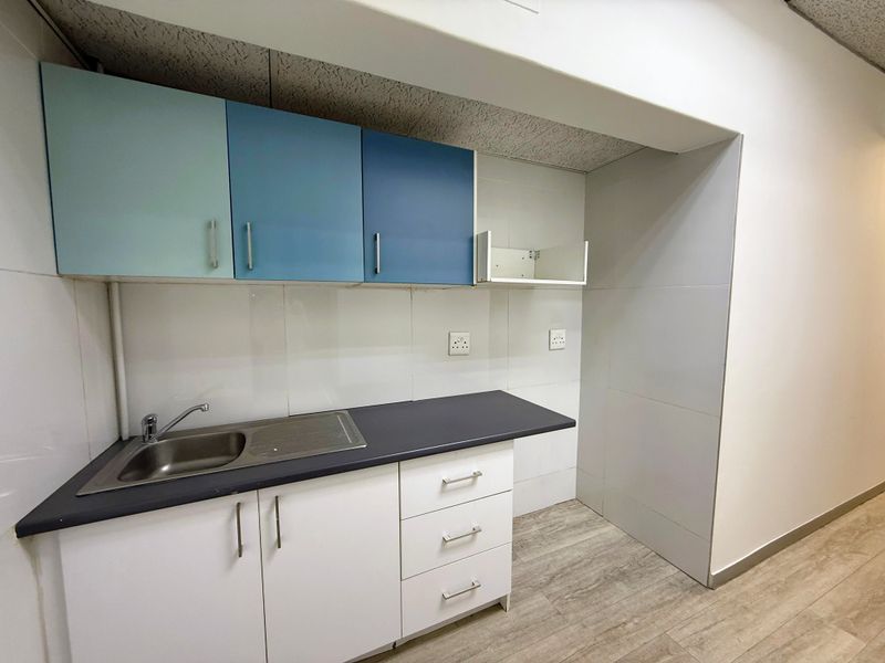 A compact office kitchenette featuring built-in cabinetry, a stainless steel sink, tiled backsplash, and wood-look flooring.