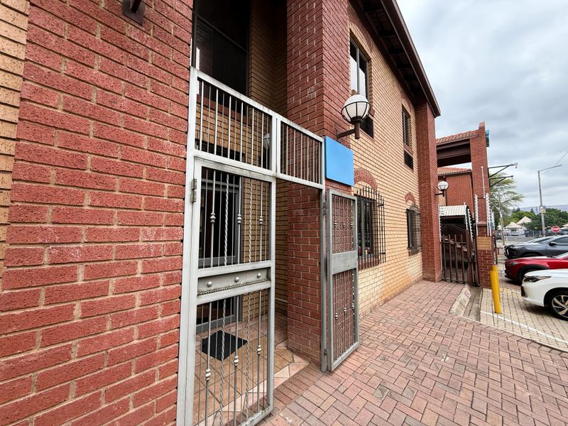 Front exterior view of a brick office building featuring a secure gated entrance and paved walkway.
