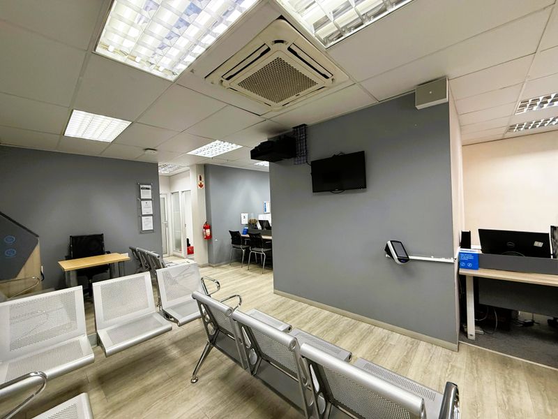 A functional office waiting area featuring a suspended ceiling, recessed lighting, cassette air conditioning, and durable laminate flooring.