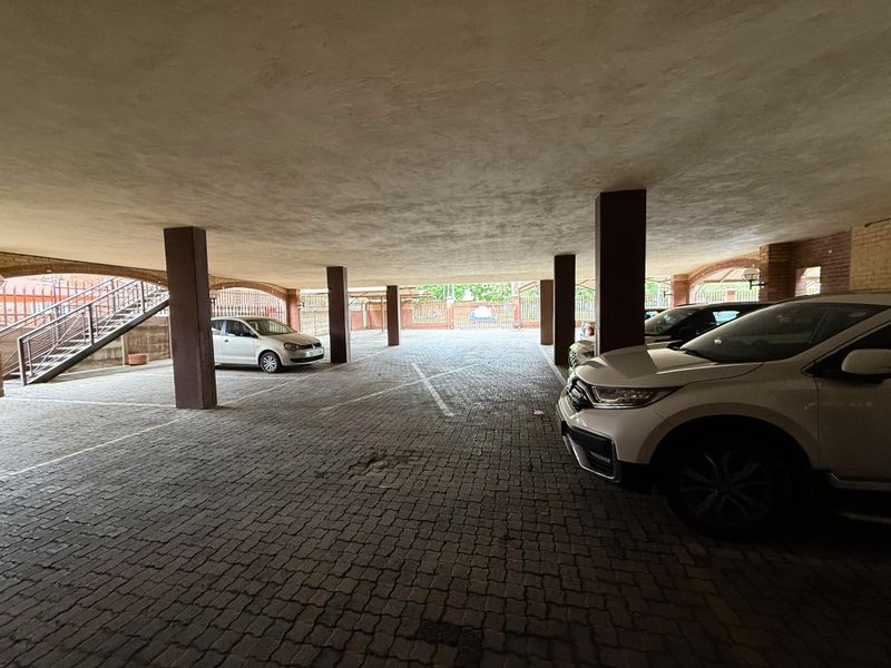 A covered parking area featuring paved ground, structural support columns, and an integrated metal staircase for building access.