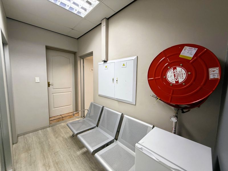 A functional office hallway featuring a wall-mounted fire hose reel, electrical distribution board, and durable laminate flooring.