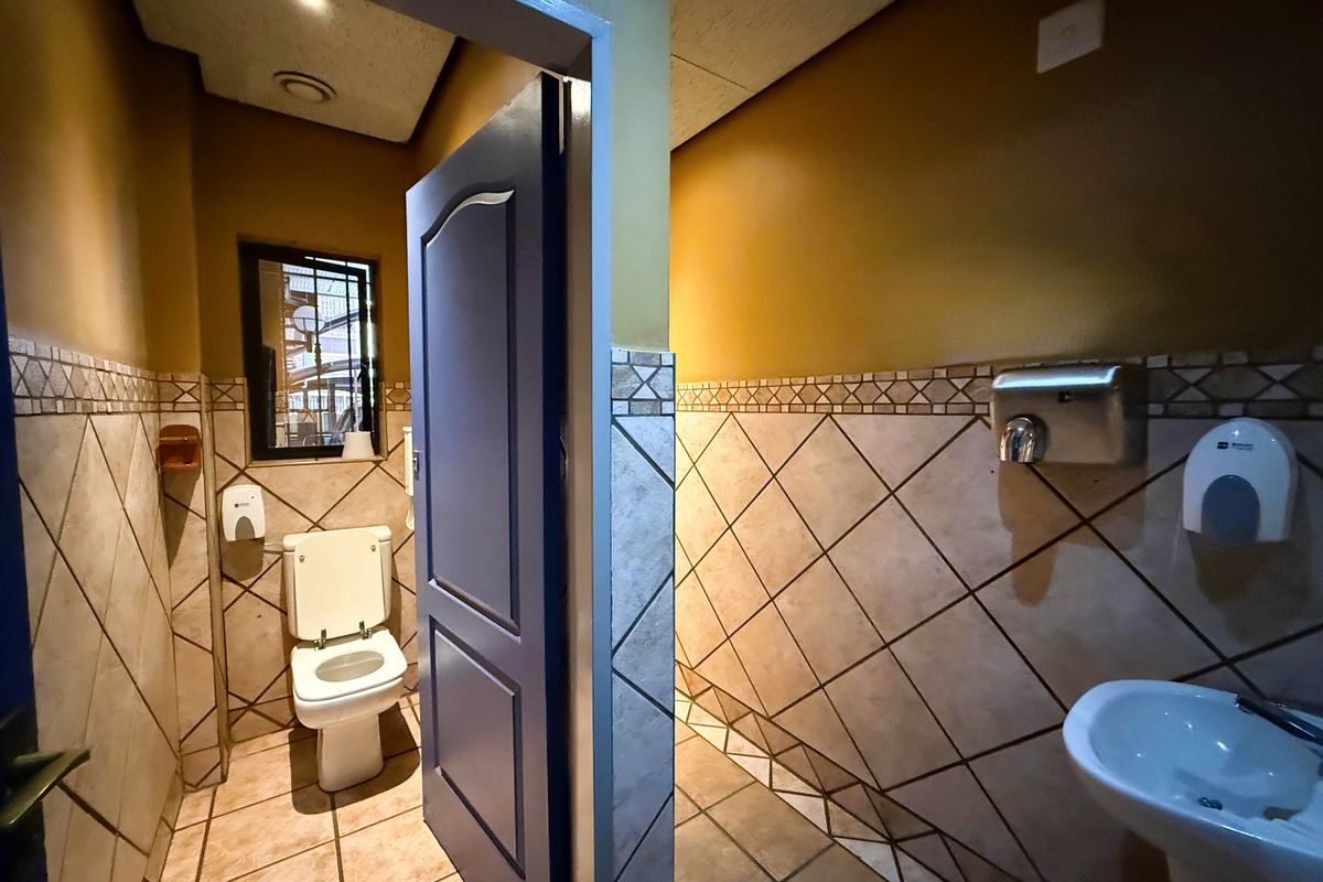 A functional office bathroom featuring ceramic tiled walls and floors, a pedestal basin, and a wall-mounted hand dryer.