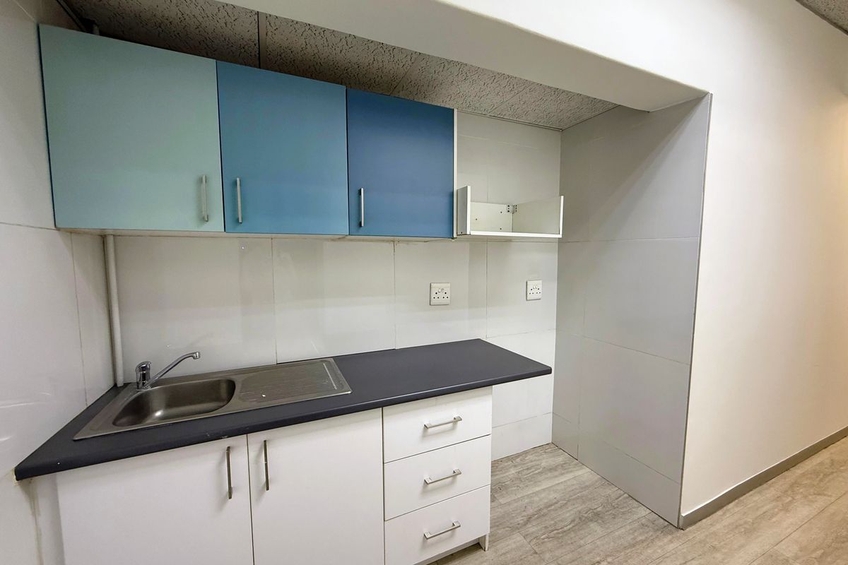 A compact office kitchenette featuring built-in cabinetry, a stainless steel sink, tiled backsplash, and wood-look flooring.