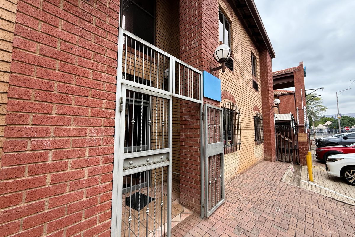 Front exterior view of a brick office building featuring a secure gated entrance and paved walkway.
