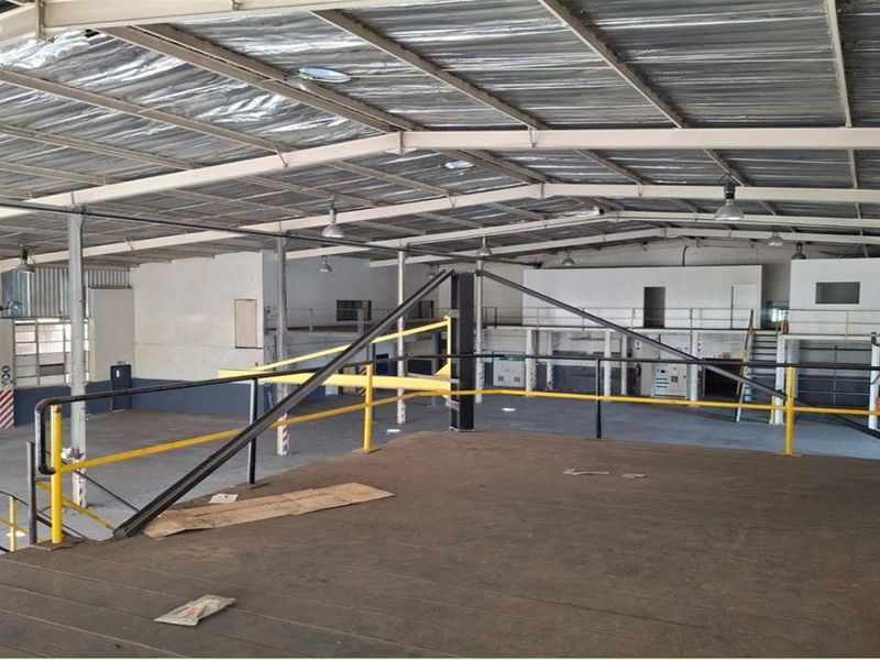 Spacious industrial warehouse featuring a mezzanine level with safety railings, exposed steel roof structure, and high-clearance ceilings suitable for various commercial or storage operations.
