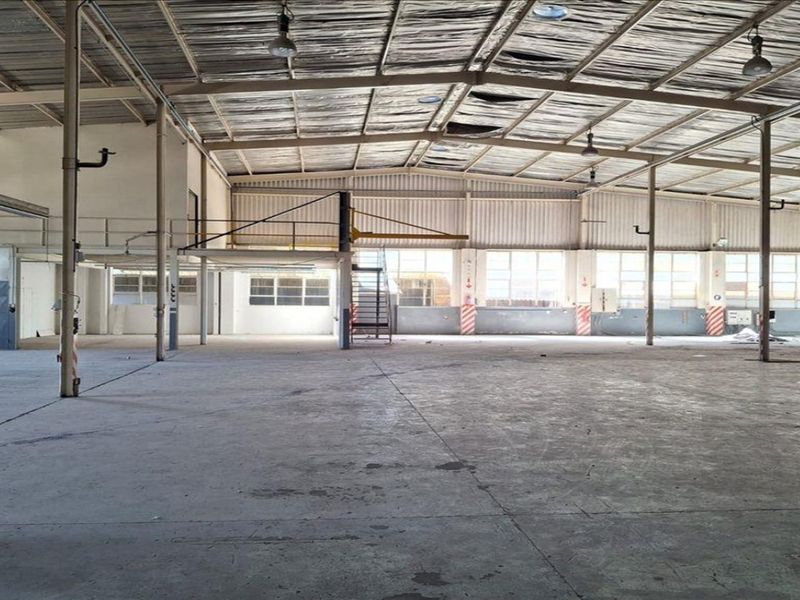 Spacious industrial warehouse featuring high ceilings, exposed steel structure, concrete flooring, and a mezzanine level with an integrated staircase.