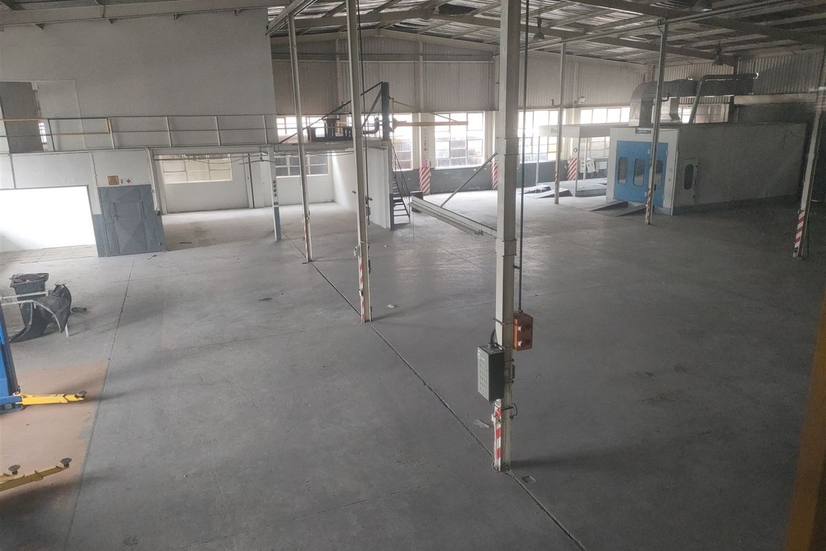 Spacious industrial warehouse featuring concrete flooring, exposed steel roof structure, mezzanine level, and a dedicated spray booth area.
