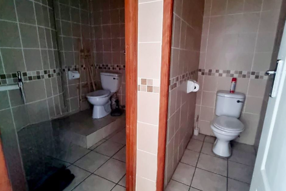A commercial bathroom facility featuring two separate toilet cubicles with tiled walls and floors, requiring cosmetic updates to modernize the space.